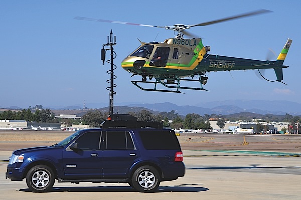 The Los Angeles County Sheriffs Department (LASD) is a Helinet Technologies customer. Here, a downlink-equipped LASD AS350 B2 hovers near a Sheriffs tactical incident downlink vehicle.