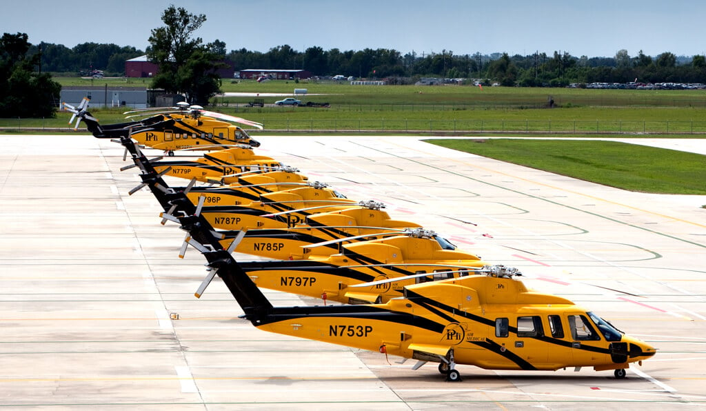 Several helicopters rest on the ground, in a row.