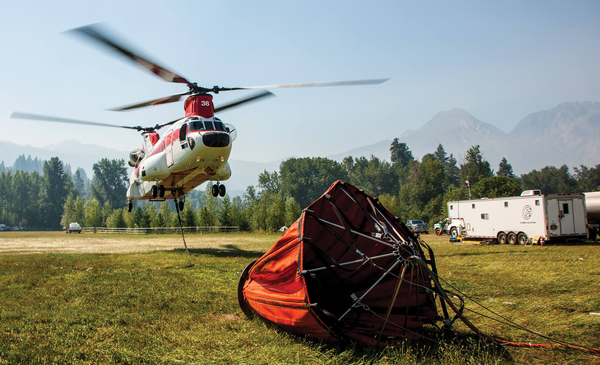 Columbia helicopter in background with firefighting bucket lying on ground
