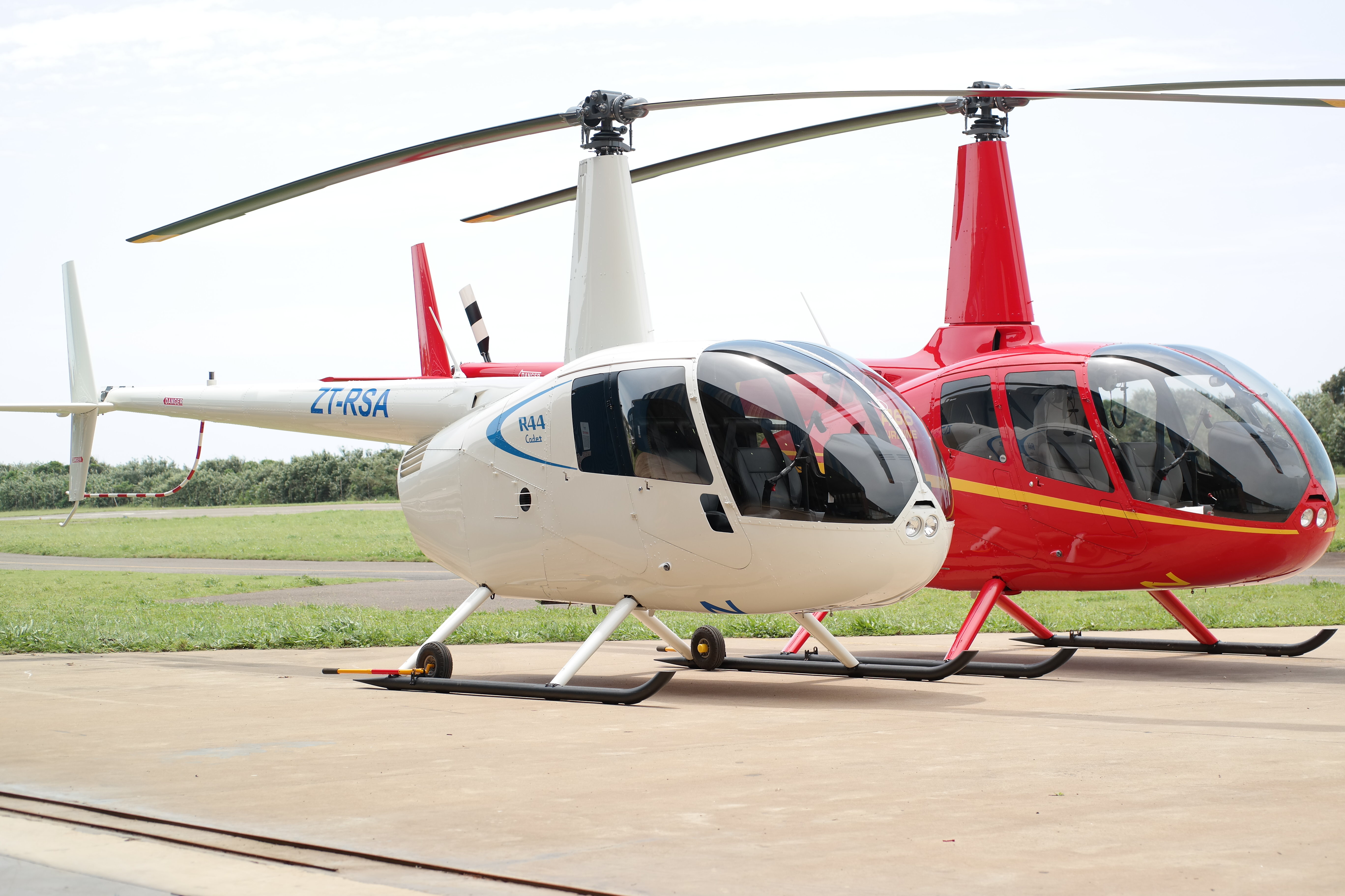 Two Robinson helicopters rest on the ground