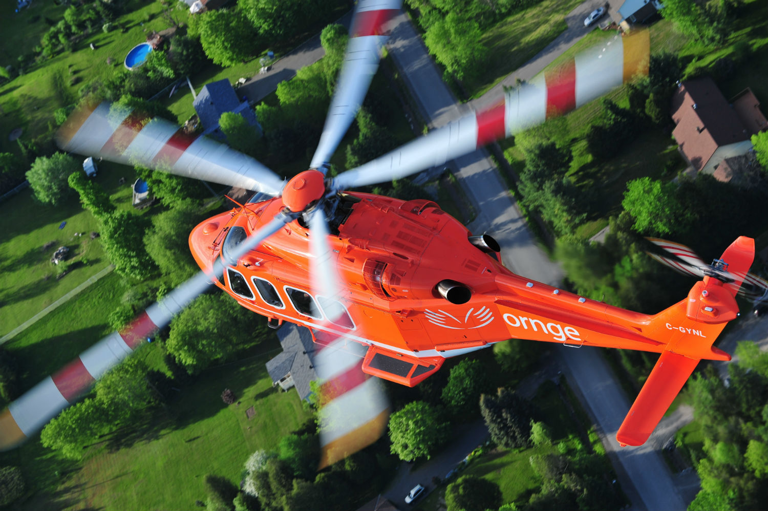 An Ornge Leonardo AW139 helicopter soars over the countryside.