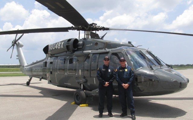 Two men stand in front of Black Hawk helicopter