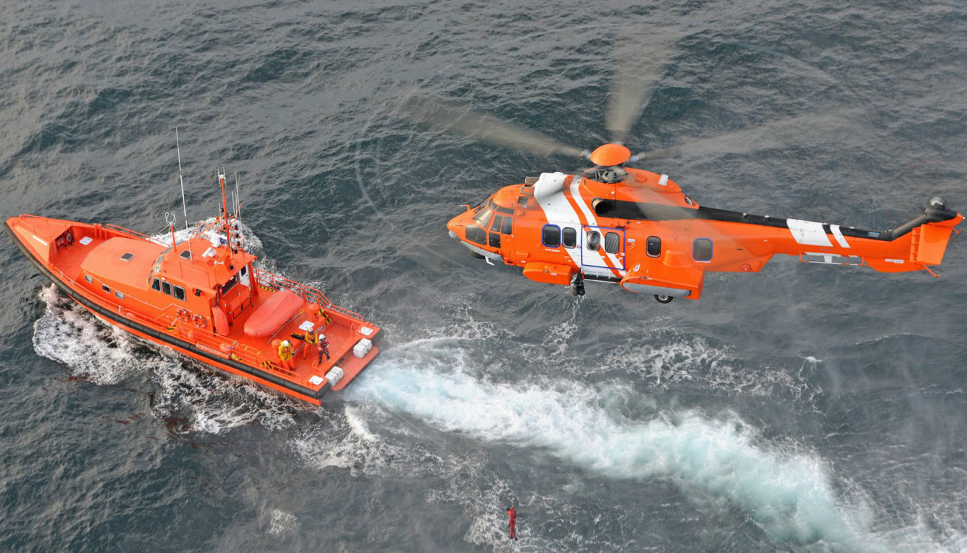 Orange H225 helicopter flies over boat and water