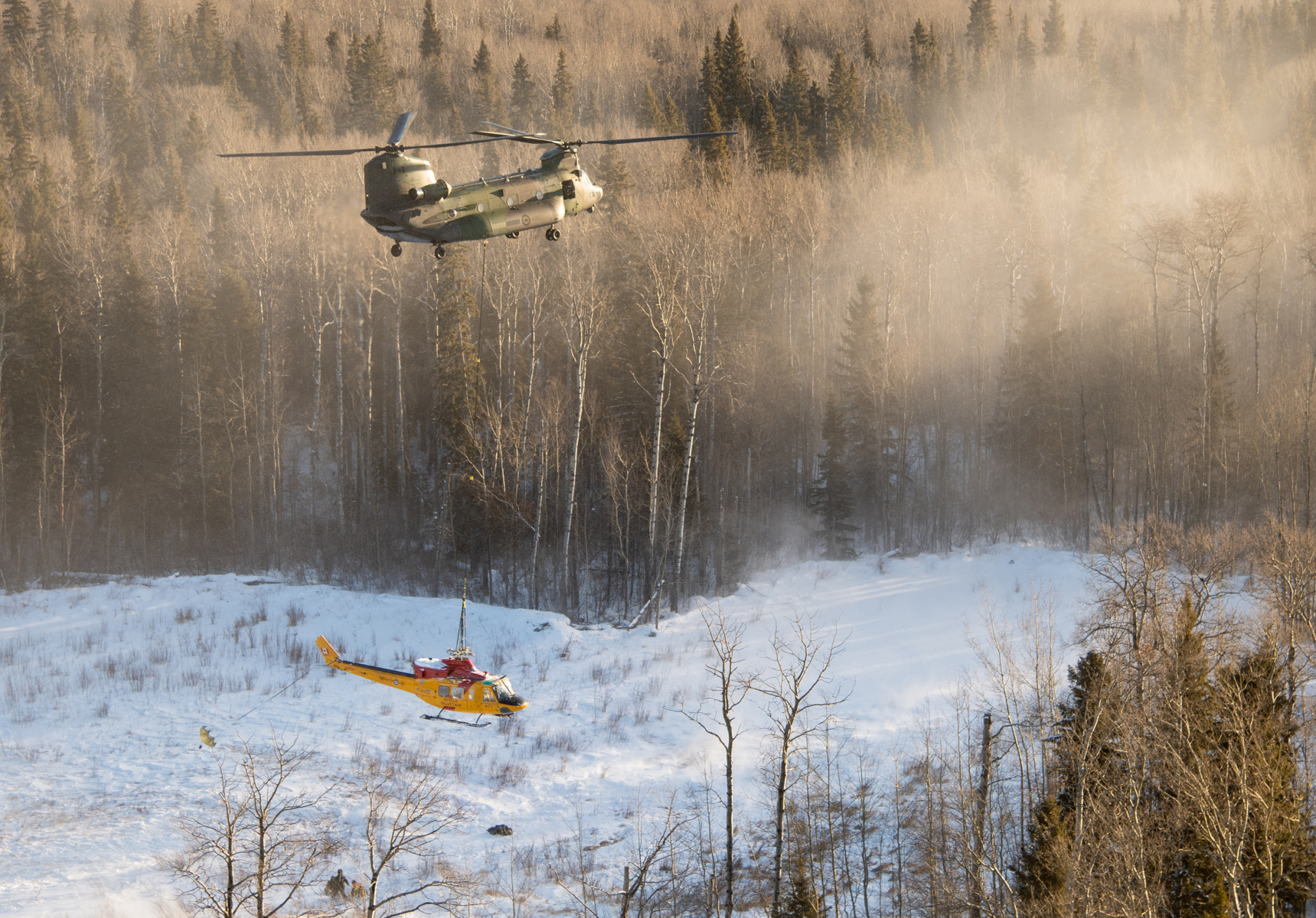 The Chinook helicopter lifts off with the Griffon slung below it. In this photo, the Griffon is not yet aligned with the Chinook and the drogue chute has not fully filled with air to steady the smaller helicopter. MCpl Amy Martin Photo