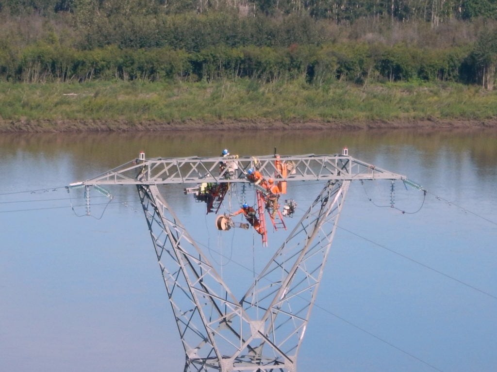 Powerline technicians attach the SkyWrap to the powerline to take the fiber optic cable across the Peace River. Slave Lake Helicopters Photo