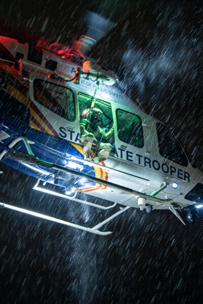 State Trooper/ pilot Jonah Nieves sits in the door of an Arizona Department of Public Safety Bell 429 as the rain pours down during night hoist training. Nieves was waiting between evolutions on a course to learn how to work as a system operator and run the hoist for night rescues. Kenan Bahadir Photo